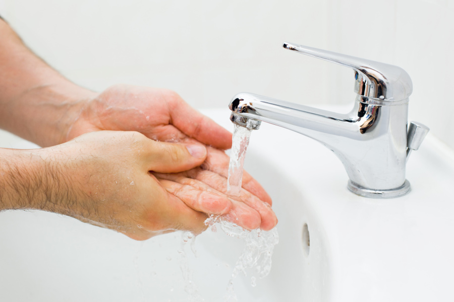 Auf diesem Bild sind Hände abgebildet, die unter einem Wasserhahn, aus dem klares Wasser fließt, gewaschen werden.
