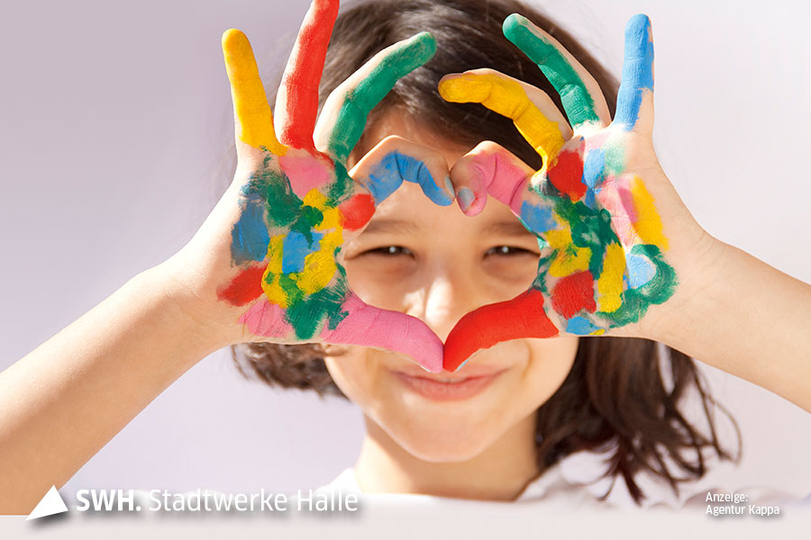 Ein Mädchen blick mit bunten Fingern in die Kamera. Die Finger formen ein Herz und die beiden Augen schauen hindurch.